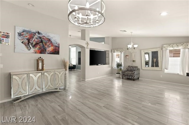 unfurnished living room with vaulted ceiling, an inviting chandelier, and light hardwood / wood-style flooring