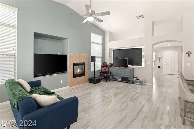 living room with ceiling fan, a wealth of natural light, lofted ceiling, and a tiled fireplace