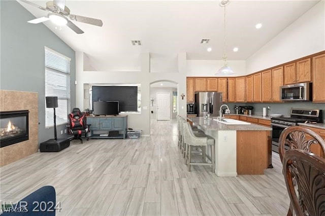 kitchen with decorative light fixtures, a kitchen bar, appliances with stainless steel finishes, an island with sink, and high vaulted ceiling