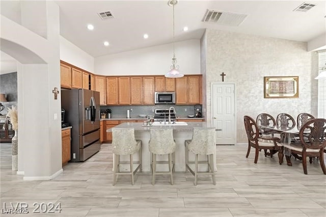 kitchen with sink, hanging light fixtures, a kitchen island with sink, appliances with stainless steel finishes, and high vaulted ceiling