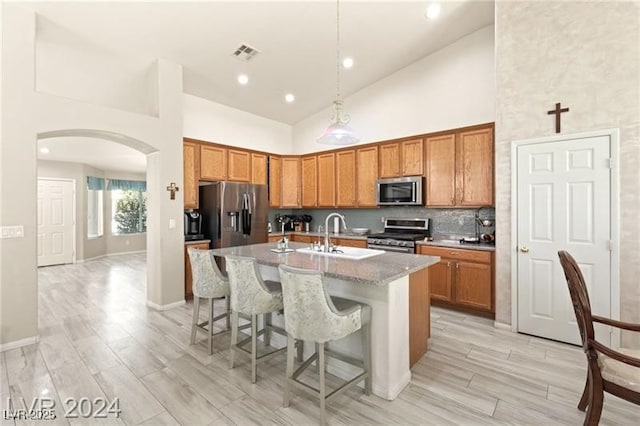 kitchen with an island with sink, appliances with stainless steel finishes, a kitchen breakfast bar, high vaulted ceiling, and sink