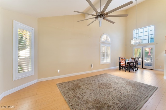 dining area featuring light hardwood / wood-style flooring, ceiling fan with notable chandelier, french doors, and high vaulted ceiling