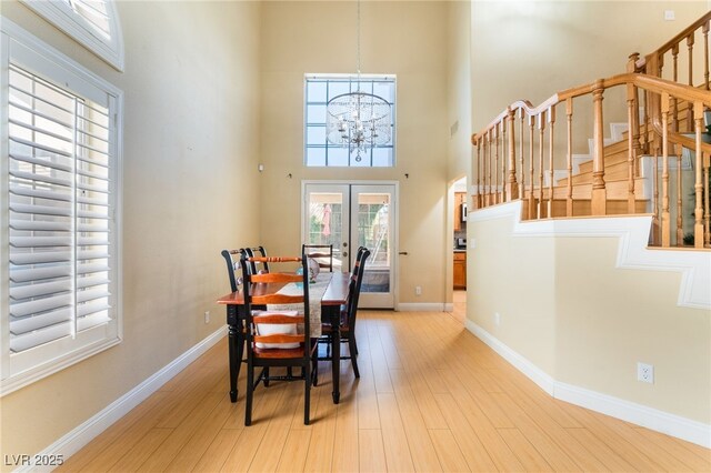 dining room featuring light hardwood / wood-style floors, a chandelier, french doors, and a towering ceiling