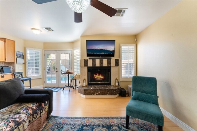 living room featuring a premium fireplace, ceiling fan, light hardwood / wood-style flooring, and french doors