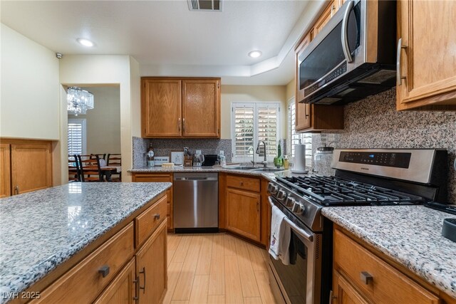 kitchen with light hardwood / wood-style floors, appliances with stainless steel finishes, a notable chandelier, light stone countertops, and sink