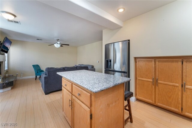 kitchen with stainless steel fridge with ice dispenser, a kitchen island, light hardwood / wood-style floors, and a breakfast bar