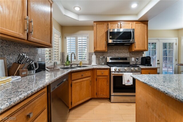 kitchen featuring light stone countertops, stainless steel appliances, french doors, decorative backsplash, and sink