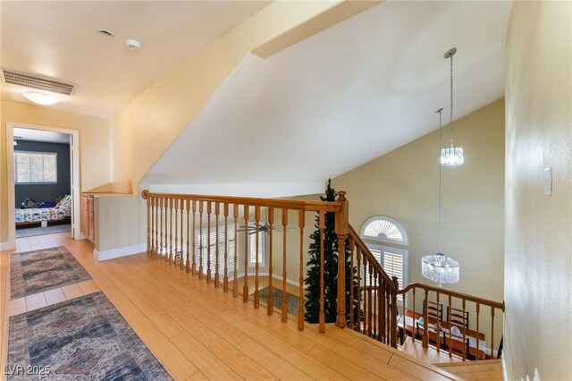 stairway with an inviting chandelier, lofted ceiling, and wood-type flooring