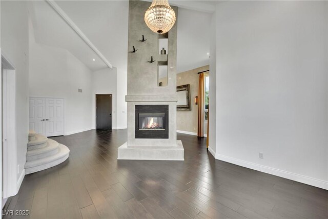 unfurnished living room featuring high vaulted ceiling, a large fireplace, dark hardwood / wood-style flooring, and an inviting chandelier