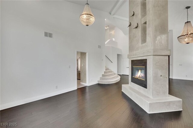 unfurnished living room featuring a towering ceiling, a premium fireplace, beamed ceiling, an inviting chandelier, and dark hardwood / wood-style floors