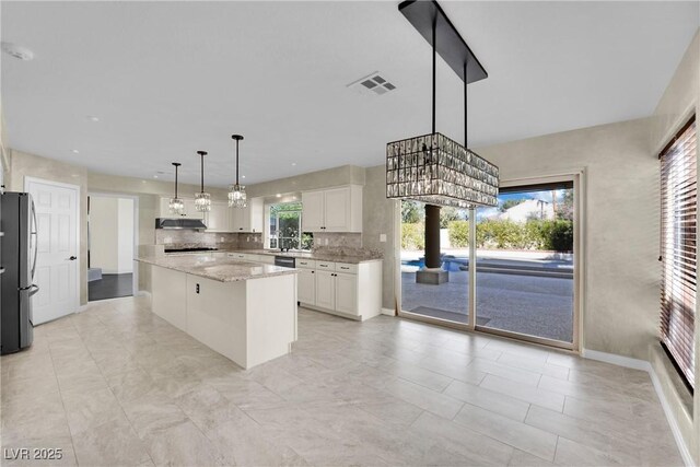 kitchen with stainless steel fridge, backsplash, a kitchen island, pendant lighting, and white cabinets