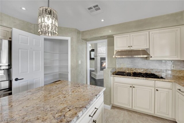 kitchen featuring stainless steel fridge with ice dispenser, black gas cooktop, hanging light fixtures, a chandelier, and light stone counters