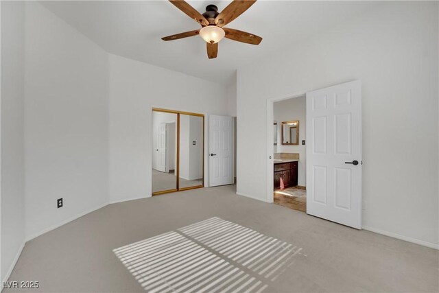 unfurnished bedroom featuring light carpet, a closet, connected bathroom, and ceiling fan