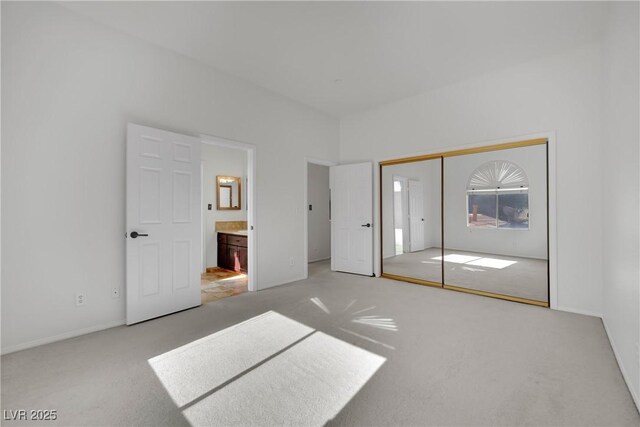 unfurnished bedroom featuring ensuite bathroom, light colored carpet, and a closet