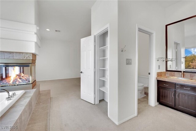 bathroom featuring tiled bath, toilet, a multi sided fireplace, and vanity