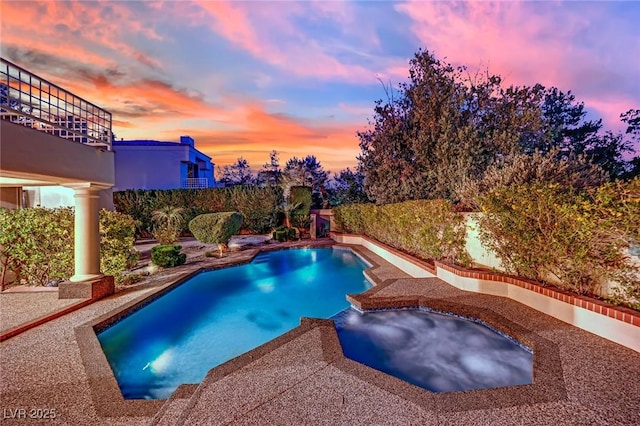 pool at dusk featuring an in ground hot tub