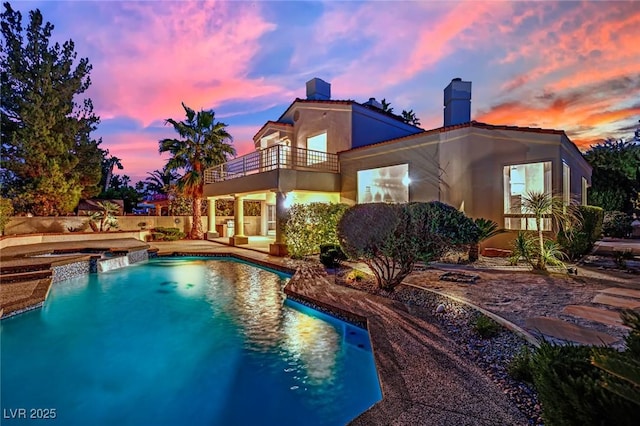 pool at dusk featuring a patio and an in ground hot tub