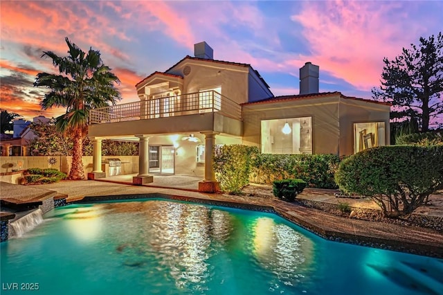 pool at dusk featuring exterior kitchen, pool water feature, and a patio