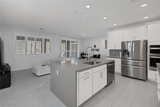 kitchen with white cabinetry, a center island with sink, stainless steel appliances, decorative backsplash, and sink