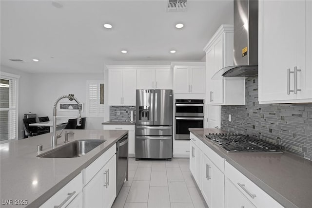 kitchen with tasteful backsplash, wall chimney range hood, sink, white cabinetry, and appliances with stainless steel finishes