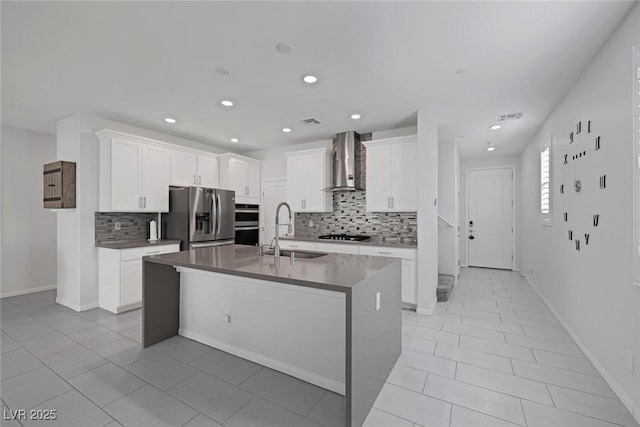 kitchen with white cabinetry, an island with sink, appliances with stainless steel finishes, wall chimney range hood, and sink