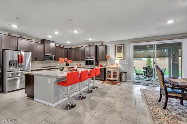 kitchen with stainless steel appliances, tasteful backsplash, a kitchen island with sink, a kitchen breakfast bar, and dark brown cabinetry