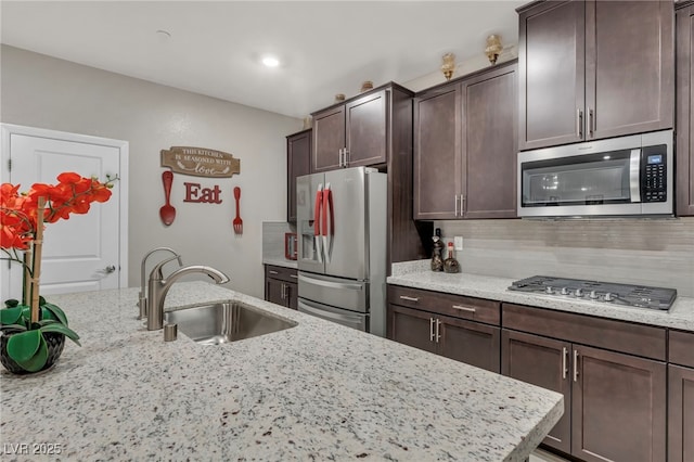 kitchen with light stone countertops, sink, stainless steel appliances, and dark brown cabinetry