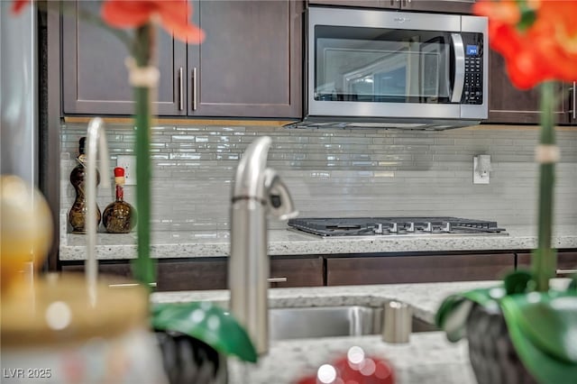 room details with decorative backsplash, dark brown cabinets, and light stone counters