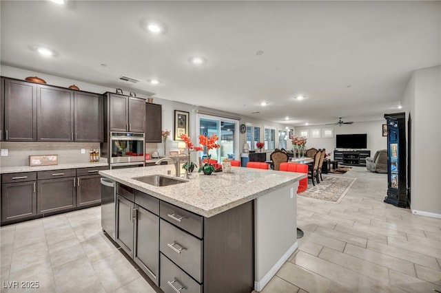 kitchen featuring an island with sink, ceiling fan, stainless steel appliances, dark brown cabinets, and sink