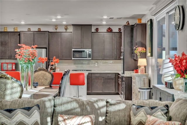 kitchen featuring appliances with stainless steel finishes, dark brown cabinets, backsplash, and light stone counters