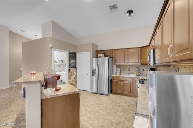 kitchen with appliances with stainless steel finishes, decorative backsplash, sink, light tile patterned floors, and a center island with sink