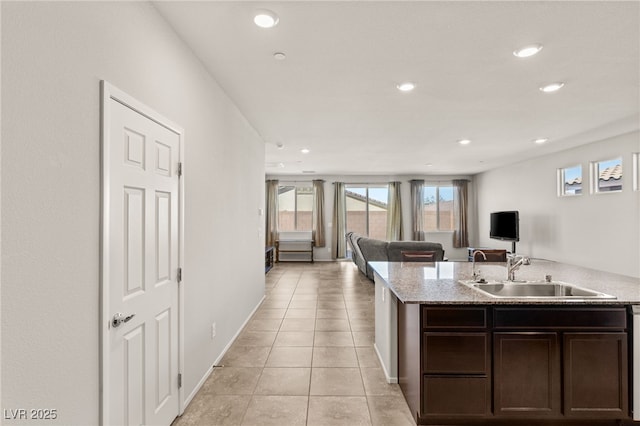 kitchen featuring light tile patterned floors, light stone counters, dark brown cabinetry, and sink