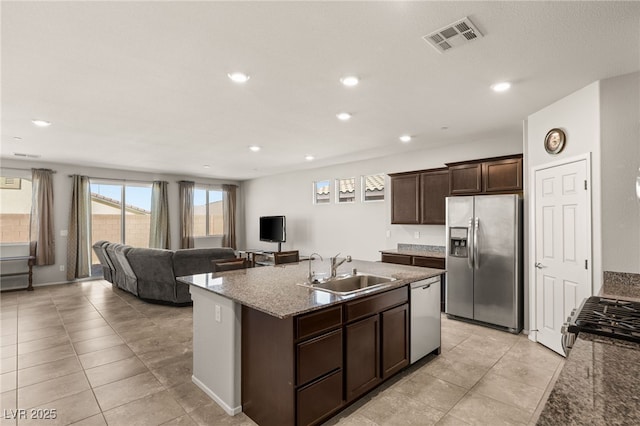 kitchen featuring light stone countertops, dark brown cabinetry, stainless steel appliances, sink, and a kitchen island with sink