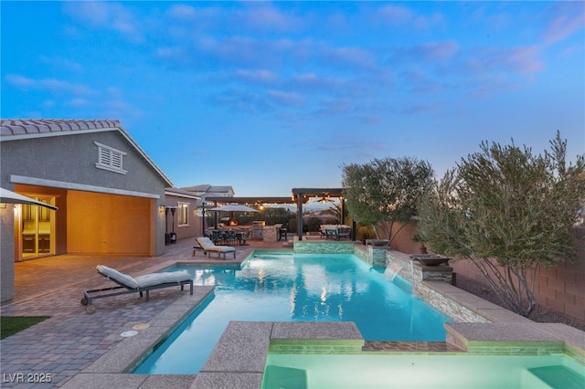 pool at dusk with exterior kitchen, a patio area, an in ground hot tub, an outdoor bar, and pool water feature