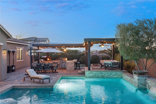 pool at dusk featuring pool water feature, exterior bar, area for grilling, and a patio