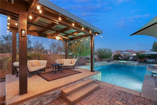 pool at dusk featuring pool water feature, a mountain view, outdoor lounge area, and a patio