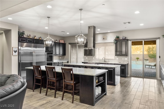 kitchen with island exhaust hood, stainless steel appliances, a center island, decorative light fixtures, and sink