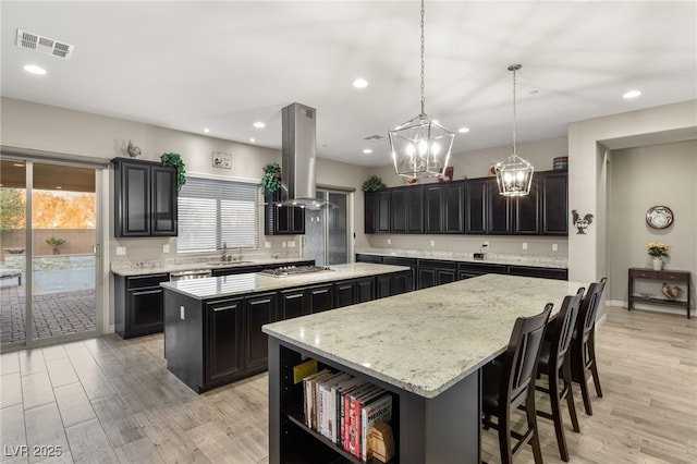 kitchen with a kitchen island, a healthy amount of sunlight, sink, hanging light fixtures, and island range hood