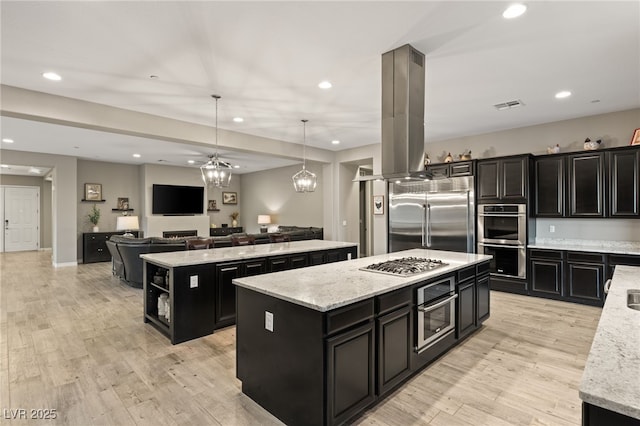 kitchen featuring appliances with stainless steel finishes, light wood-type flooring, a kitchen island, pendant lighting, and light stone counters