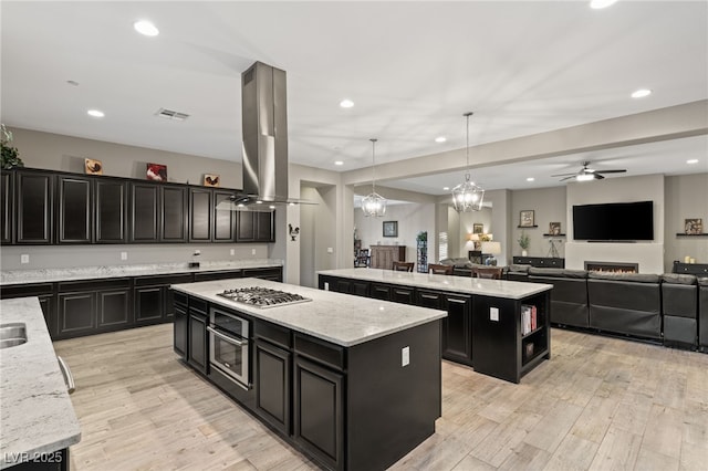 kitchen with a center island, island exhaust hood, hanging light fixtures, light wood-type flooring, and ceiling fan with notable chandelier