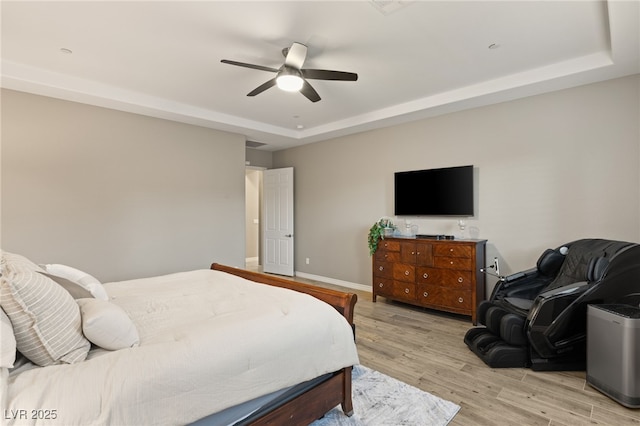 bedroom with ceiling fan, light wood-type flooring, and a tray ceiling