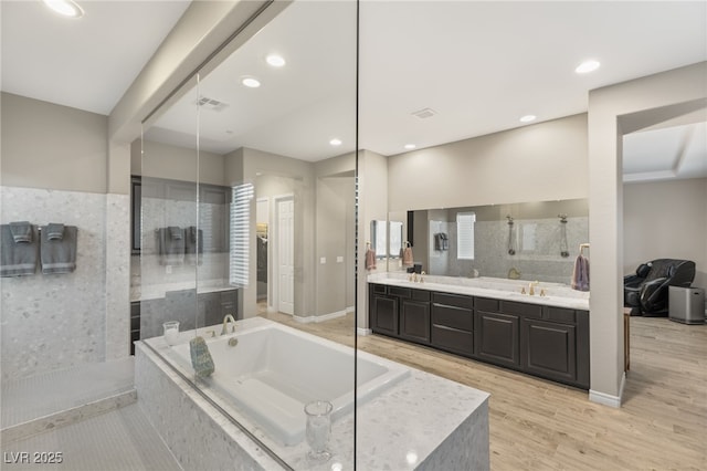 bathroom with a relaxing tiled tub, hardwood / wood-style flooring, and vanity