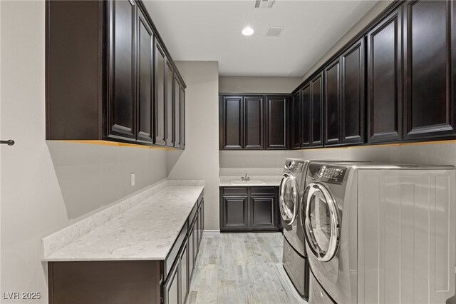 clothes washing area featuring washer and clothes dryer, sink, light hardwood / wood-style flooring, and cabinets