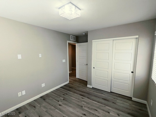 unfurnished bedroom with dark wood-type flooring, a closet, and a notable chandelier