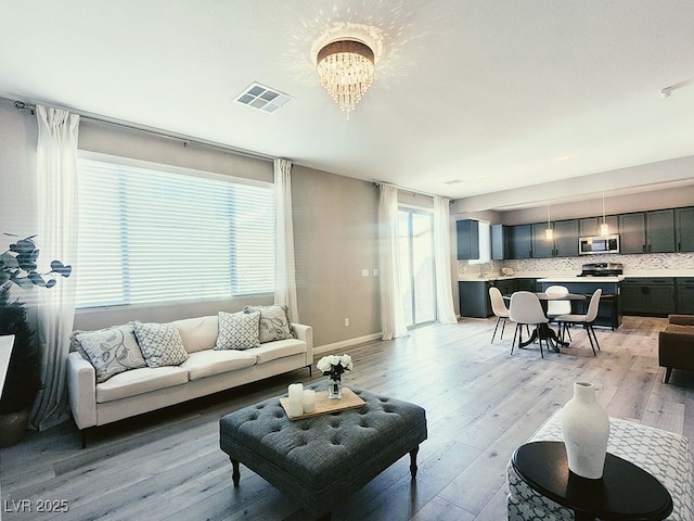 living room with an inviting chandelier, a healthy amount of sunlight, and light hardwood / wood-style flooring