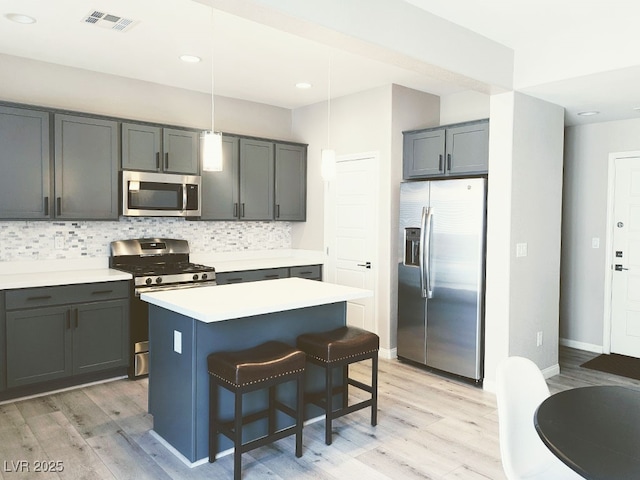 kitchen featuring appliances with stainless steel finishes, backsplash, hanging light fixtures, a kitchen island, and light hardwood / wood-style flooring