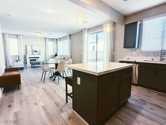 kitchen featuring pendant lighting, a kitchen island, decorative backsplash, sink, and light wood-type flooring