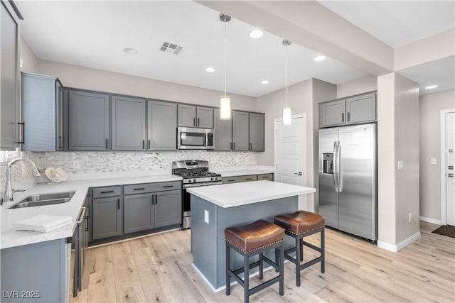 kitchen featuring sink, gray cabinets, appliances with stainless steel finishes, hanging light fixtures, and a kitchen island