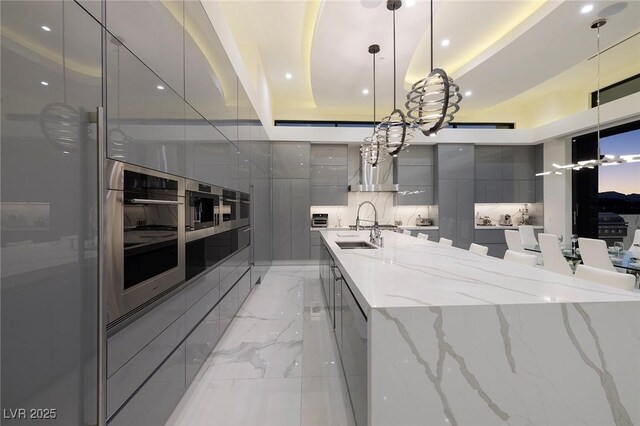 kitchen with pendant lighting, sink, gray cabinets, a raised ceiling, and light stone counters