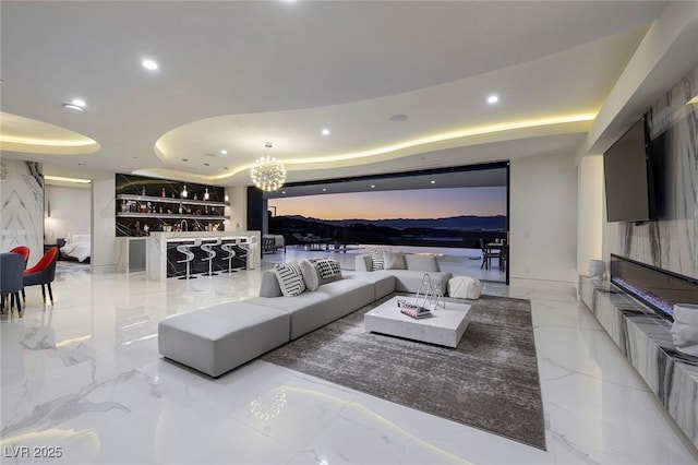 living room with an inviting chandelier, a raised ceiling, and bar area